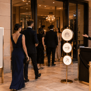 Invités accueillis à l’entrée d’un événement avec signalétique élégante et hôtesse orientant le parcours